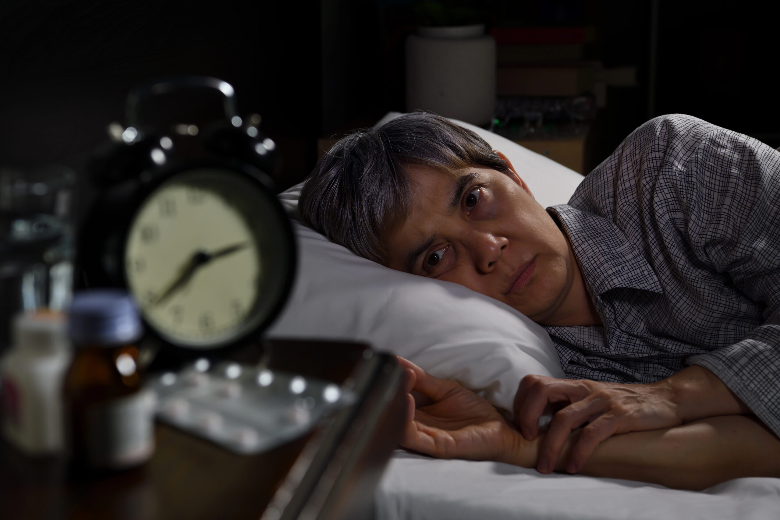 woman over 50 laying awake in bed looking at her clock 