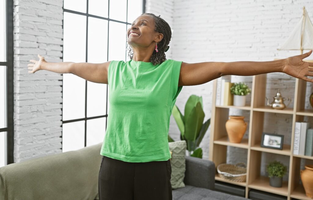Woman standing in her living room with arms open, appearing relaxed and comfortable while moving at home